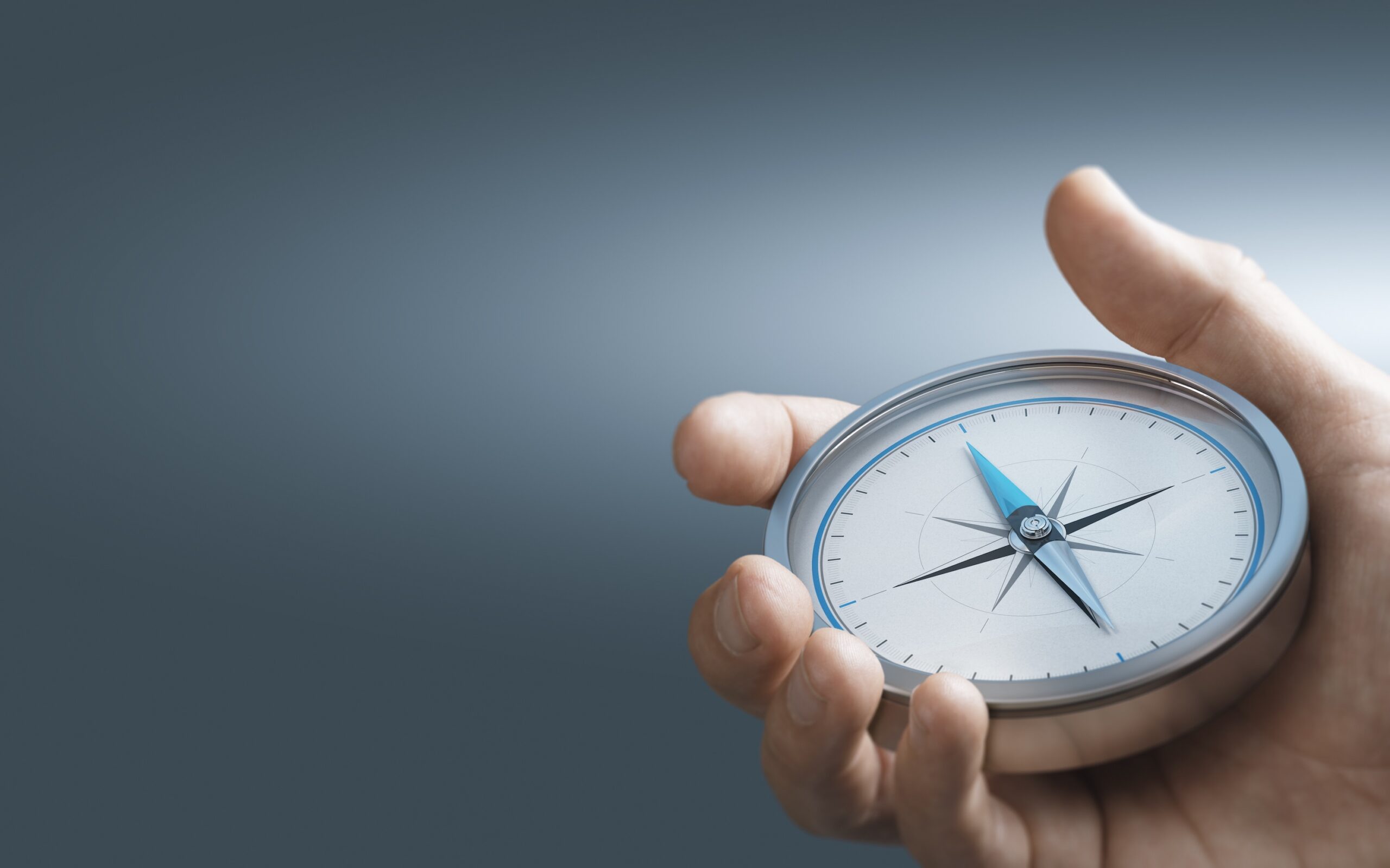 Hand holding a compass over blue background with copy space. Concept of Strategic orientation in business or marketing. Composite image between a 3d illustration and a photography.